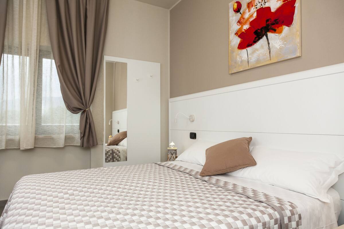 A neatly made bed with a checkered bedspread, a bedside table with a lamp, and a painting on the wall.