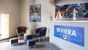 A modern hotel lobby with a 'RIVIERA HUB' sign, comfortable seating, and a wall decorated with travel-themed artwork. - Riviera Hub (Cisano sul Neva)