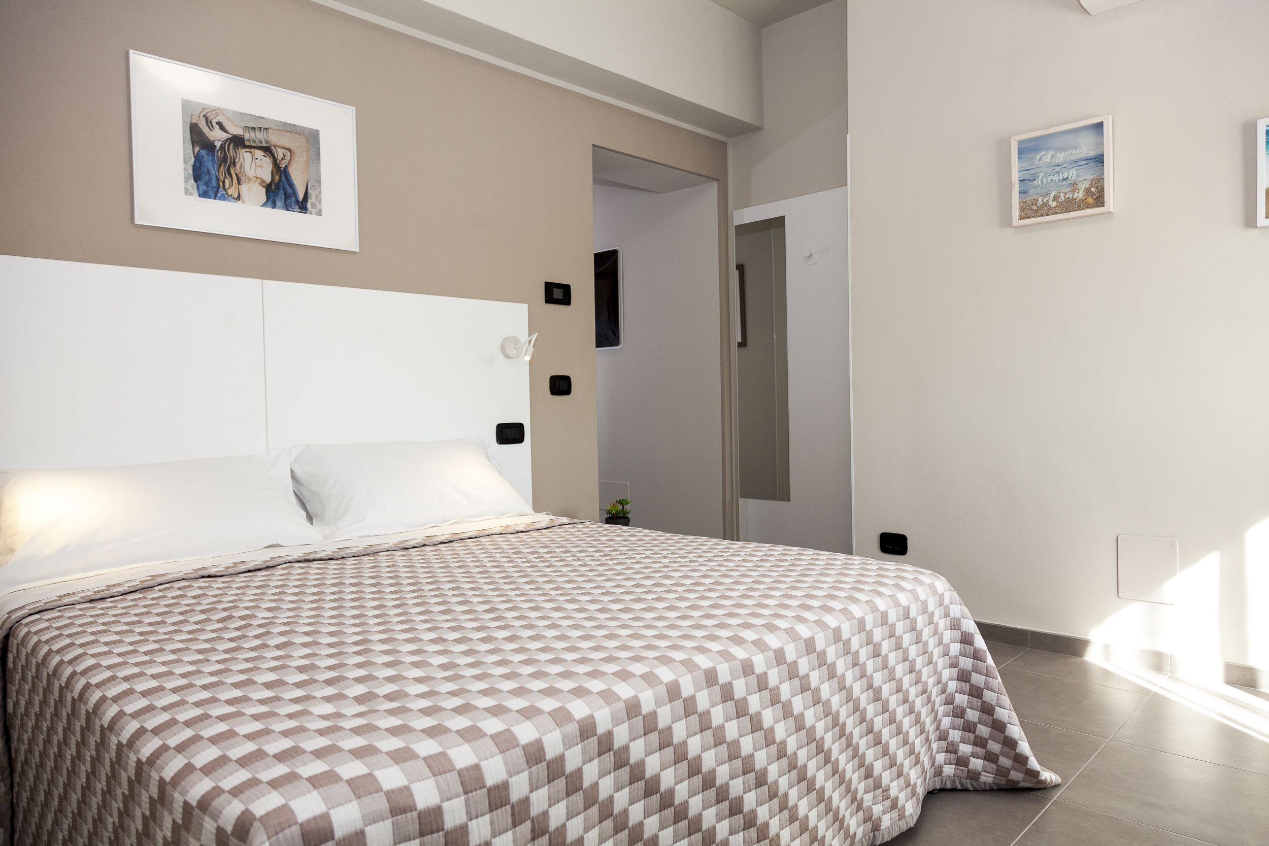 A bedroom with a checkered bedspread, a white headboard, and a framed picture on the wall.