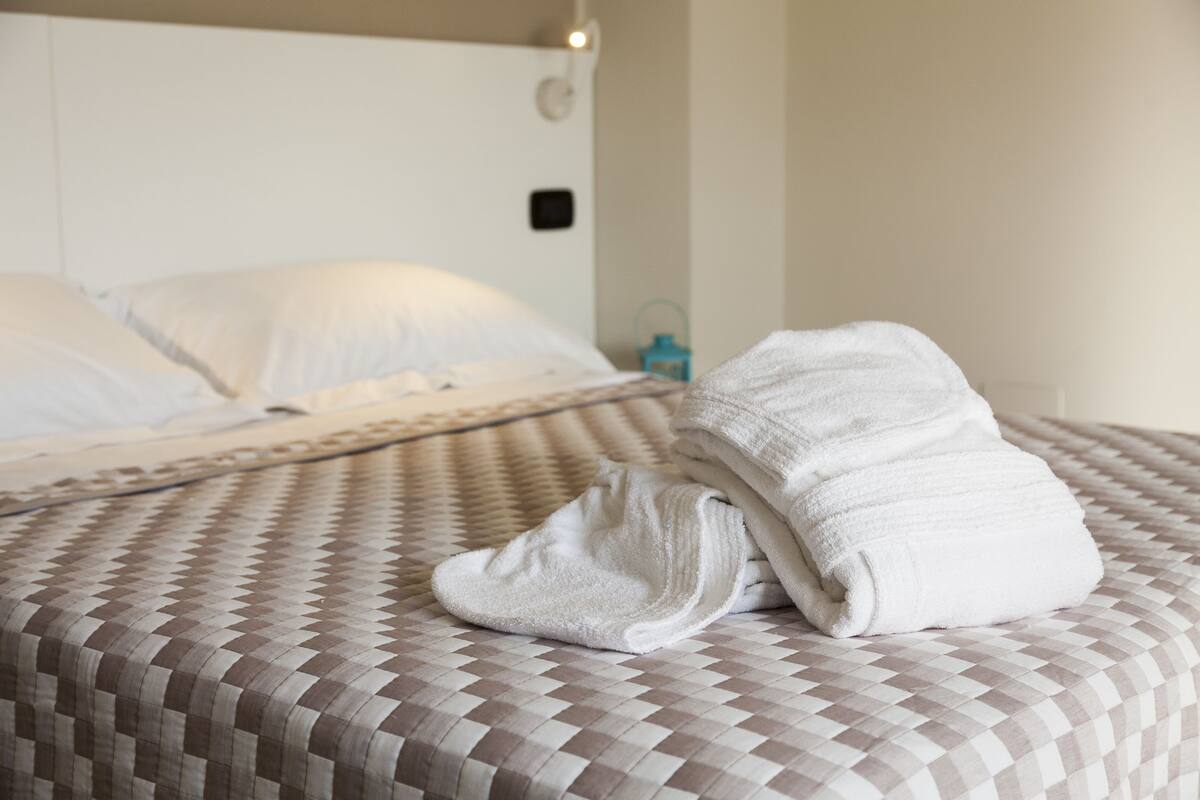 A neatly made bed with a checkered bedspread and a folded white towel on the bed.