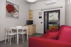 Ett kompakt vardagsrum med en matplats, en röd soffa, en tv och en dörr med utsikt.