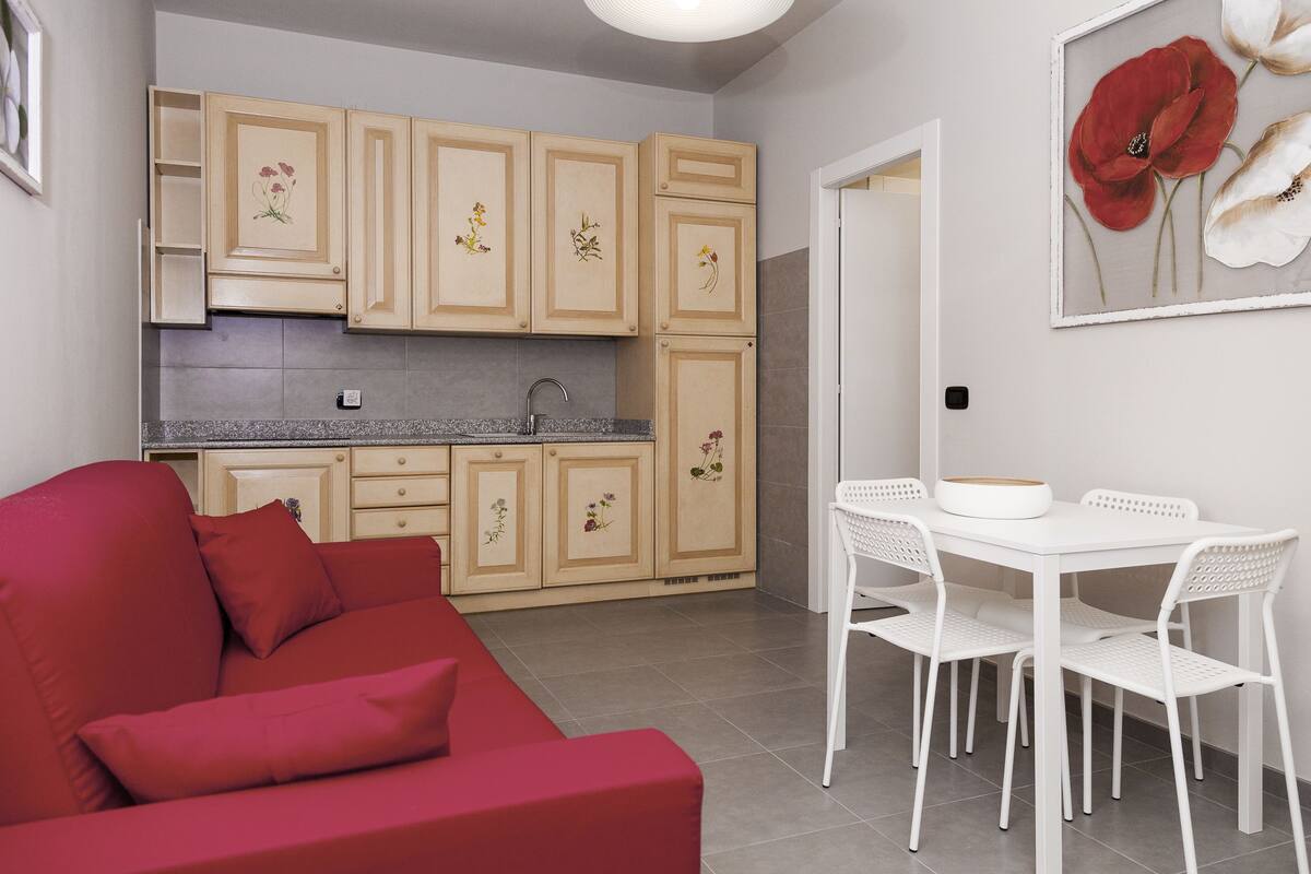 A compact living space with a kitchenette, a dining area with white chairs, and a red sofa.