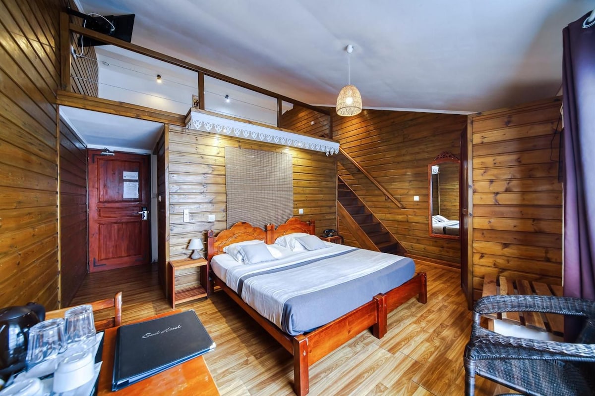 Une pièce en bois avec un lit, une chaise, un bureau et un escalier.