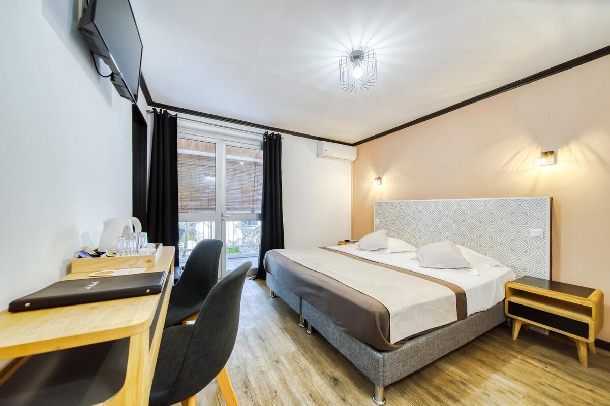 Une chambre d’hôtel avec un lit, un bureau, une chaise, une télévision et une fenêtre avec des rideaux.