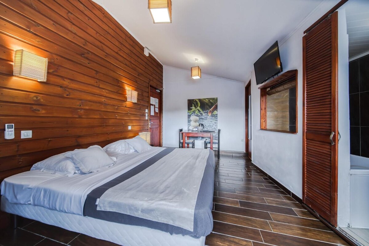 A hotel room with a wooden wall, a bed, a desk, and a TV.