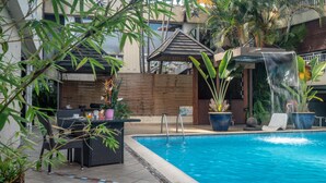 Zona de piscina con una cascada, rodeada de plantas en macetas y mobiliario exterior.