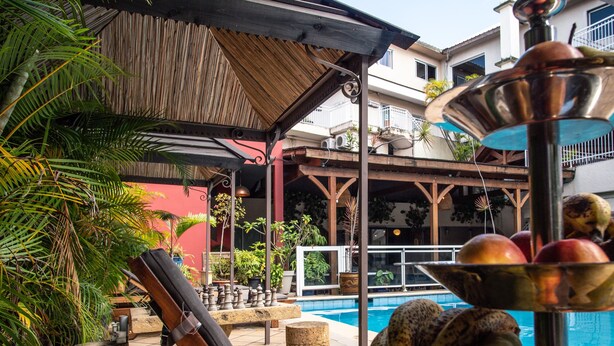 Zona junto a la piscina con una pérgola de madera, un tablero de ajedrez y un cuenco con fruta.