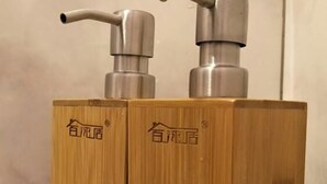 Dos dispensadores de madera con bombas metálicas sobre una repisa de metal.