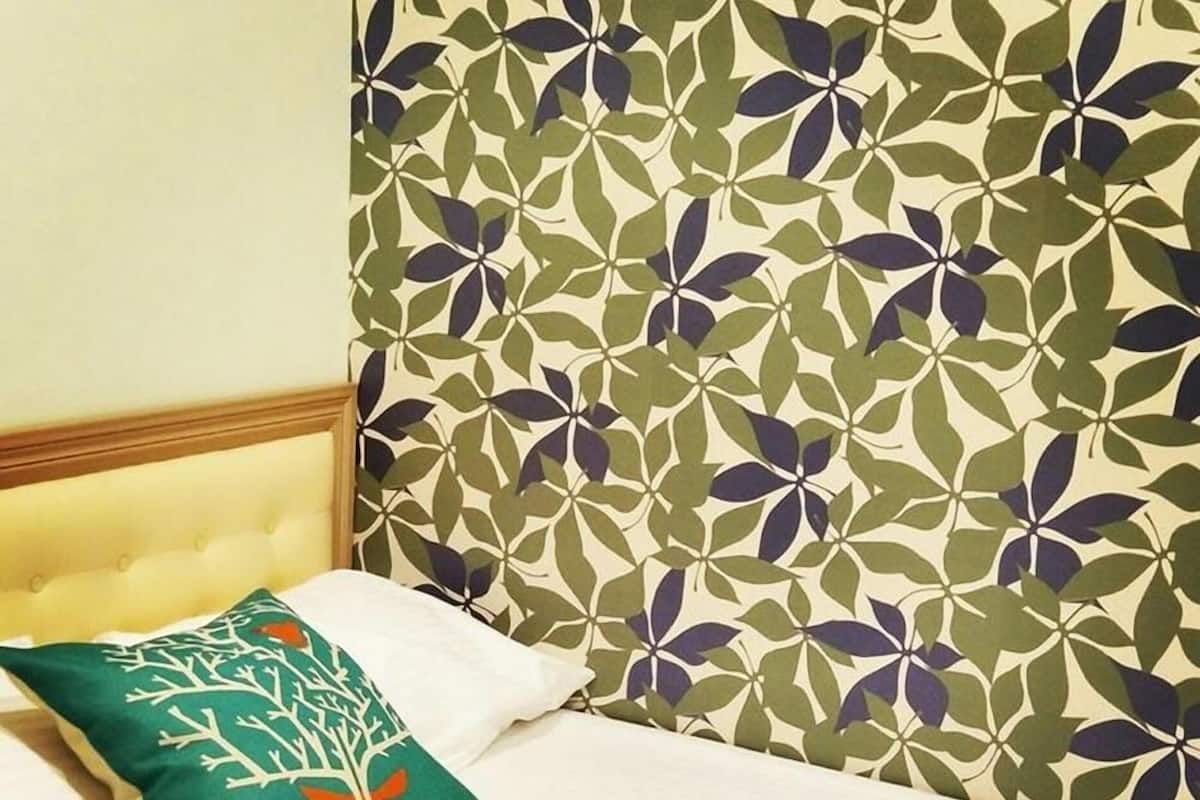 A bed with a white headboard, a green pillow with a tree and deer design, and a wall with a leafy pattern.