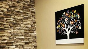 Habitación de hotel con pared de piedra, cama con ropa de cama blanca y un cuadro enmarcado de un árbol con frutos de colores.