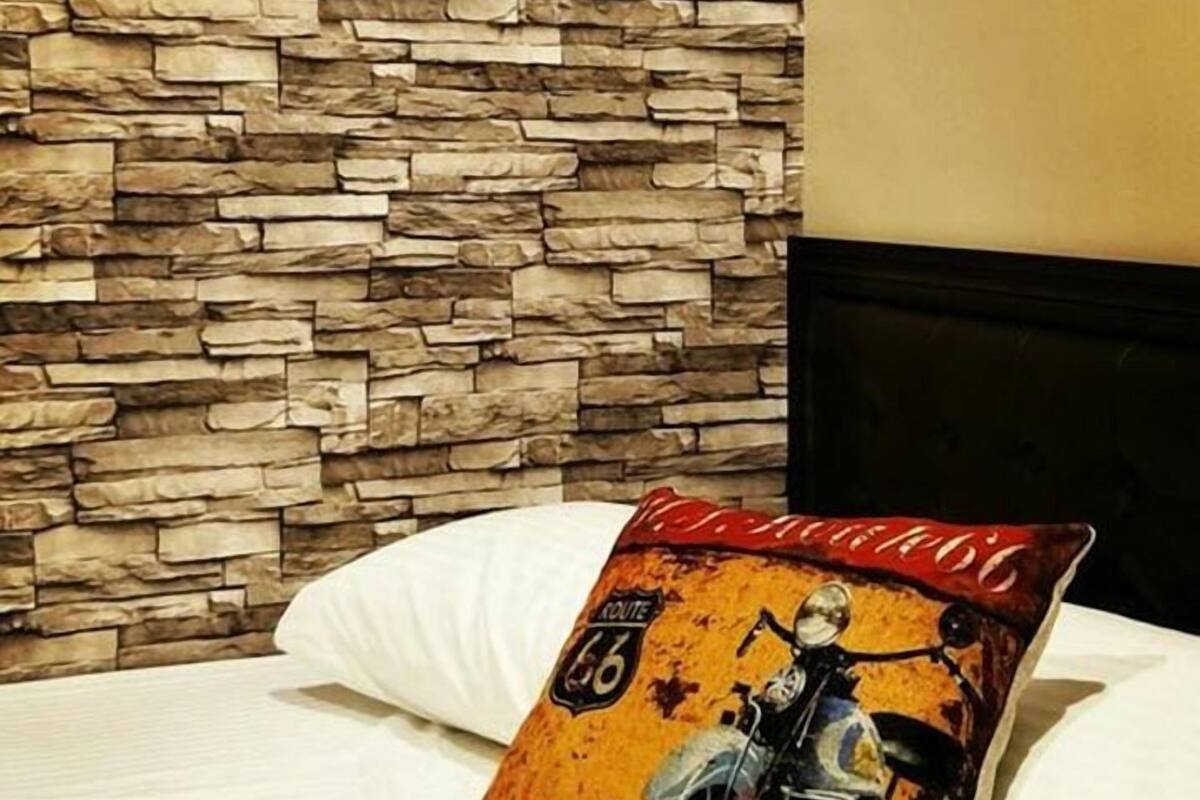 A bed with a pillow featuring a vintage motorcycle design, set against a stone wall backdrop.