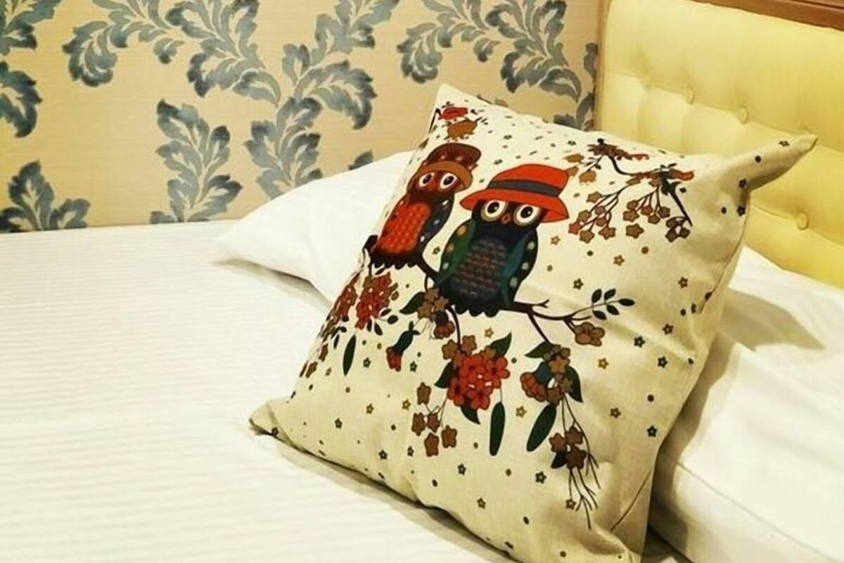 A bed with a white sheet and a decorative pillow featuring owls and flowers.