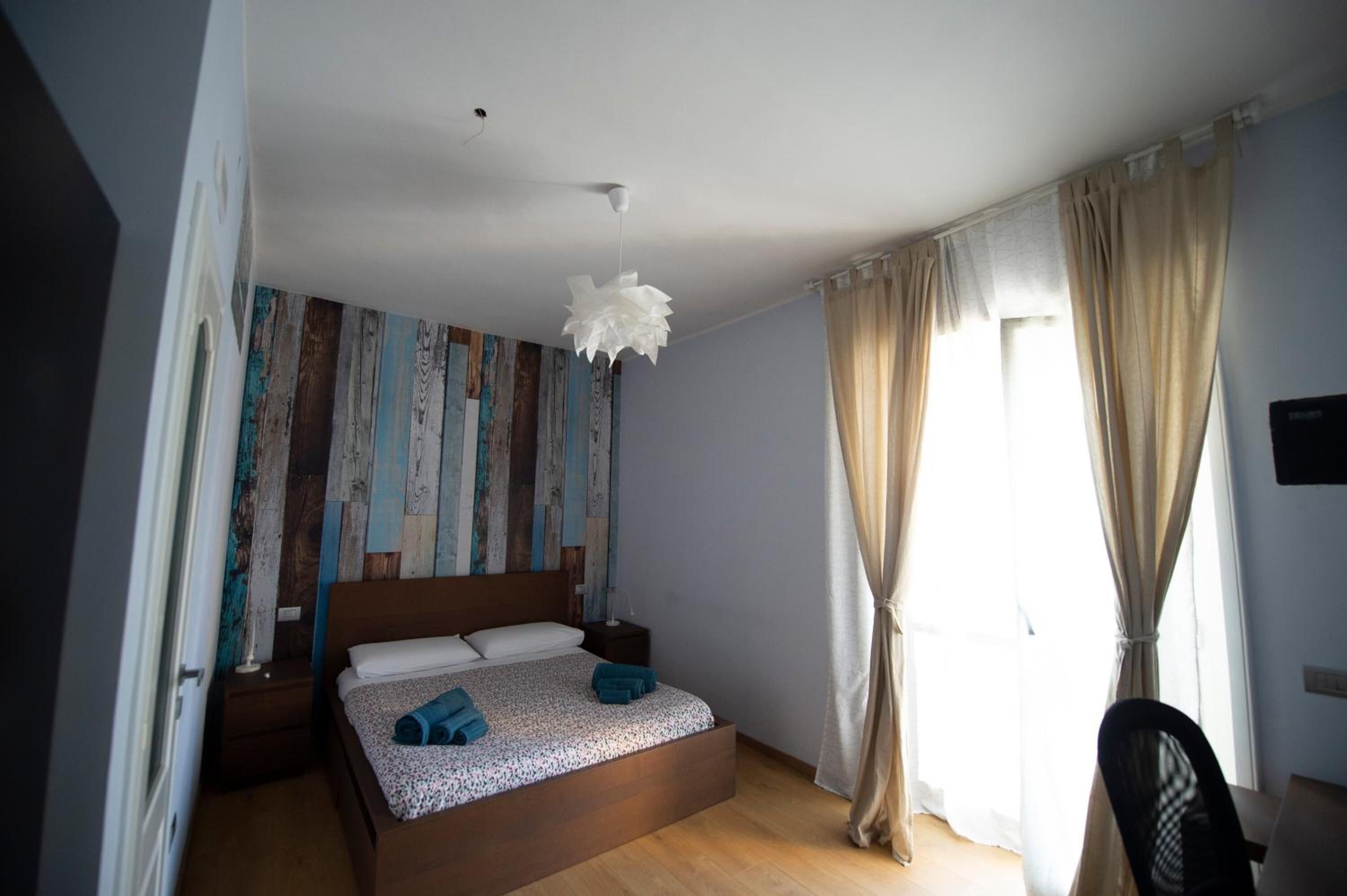 Una camera da letto con un letto di legno, un comodino, un lampadario e vista sull'esterno attraverso una finestra con tende.