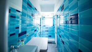 Un baño moderno con paredes de azulejos azules, un lavabo blanco y una zona de ducha.