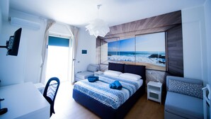 Un dormitorio moderno con una cama grande, un escritorio y una silla. Se ve una ventana con vista al océano.
