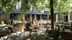 An outdoor seating area with wooden tables and chairs, surrounded by potted plants and trees. - Marias Platzl (Munich)