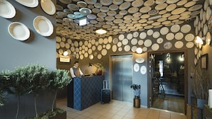 A reception area with a wall of plates, a reception desk, a potted plant, and a luggage trolley. - Marias Platzl (Munich)