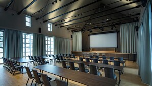 A conference room with long tables and chairs, a large screen, and a stage with curtains. - Marias Platzl (Munich)
