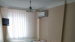 A room with two single beds, a ceiling fan, an air conditioning unit, and a TV mounted on the wall.