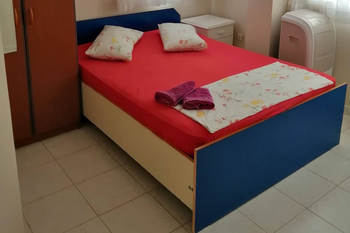 A bedroom with a bed, a nightstand, a wardrobe, a desk, and a chair.
