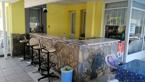 A bar area with a stone counter, two bar stools, a trash bin, and a table with a patterned tablecloth.