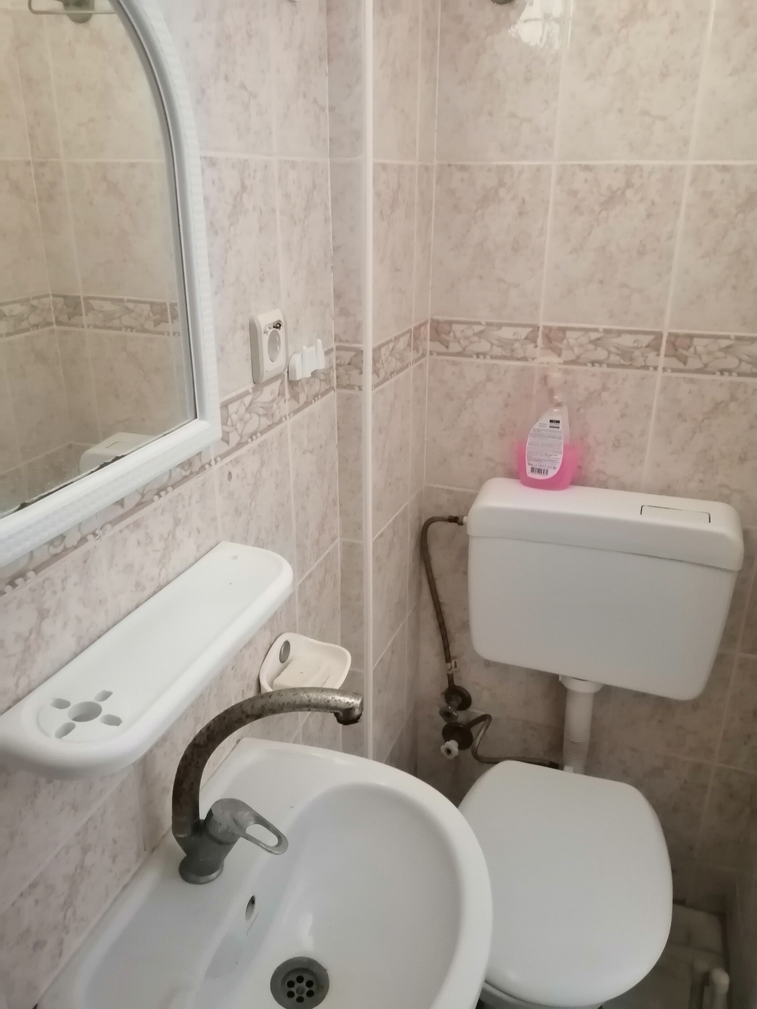 A bathroom with a white sink, a mirror, a toilet, and a soap dispenser.