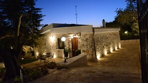 Un edificio de piedra con diseño moderno, que presenta una escalera hacia una puerta, asientos al aire libre y una entrada bien iluminada.