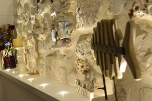 Una pared con superficie de piedra texturizada, un estante blanco con una placa y una exhibición de cubiertos.