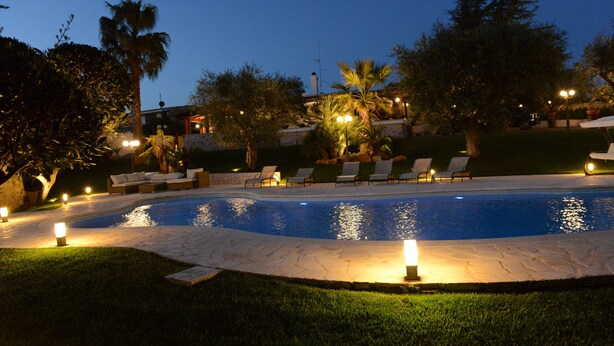 Una piscina con sillones de descanso y luces alrededor.