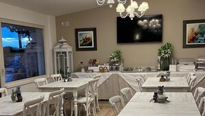 Un comedor con mesas y sillas blancas, una araña y un televisor en la pared.