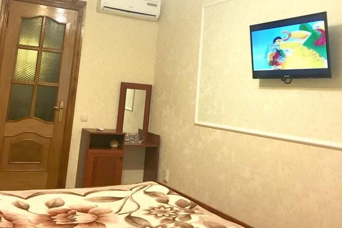 Um quarto com uma cama, televisão fixada na parede, aparelho de ar condicionado e porta de madeira.
