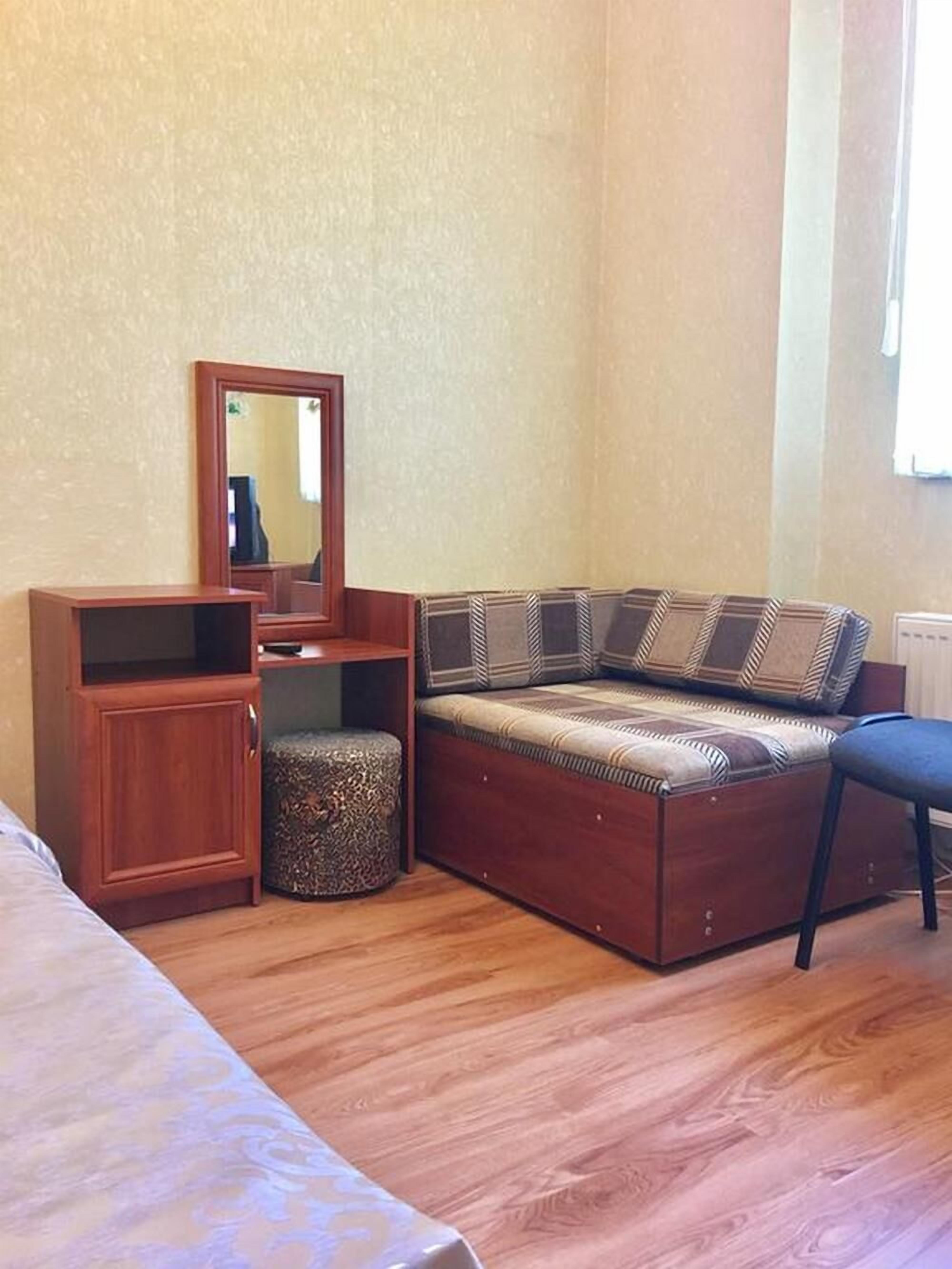 A room with a wooden cabinet, a sofa with patterned cushions, a round ottoman, and a mirror on the wall.