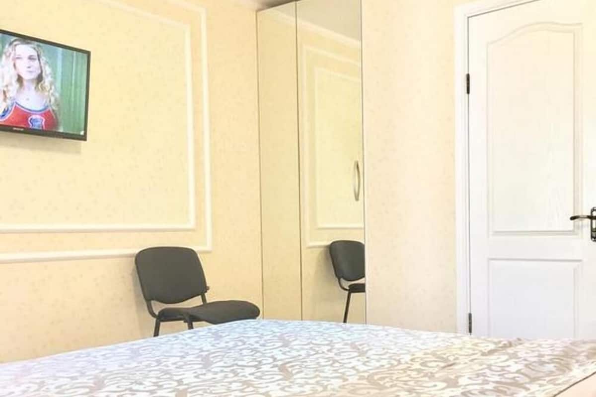 Quarto de hotel com cama, duas cadeiras, televisão e porta.