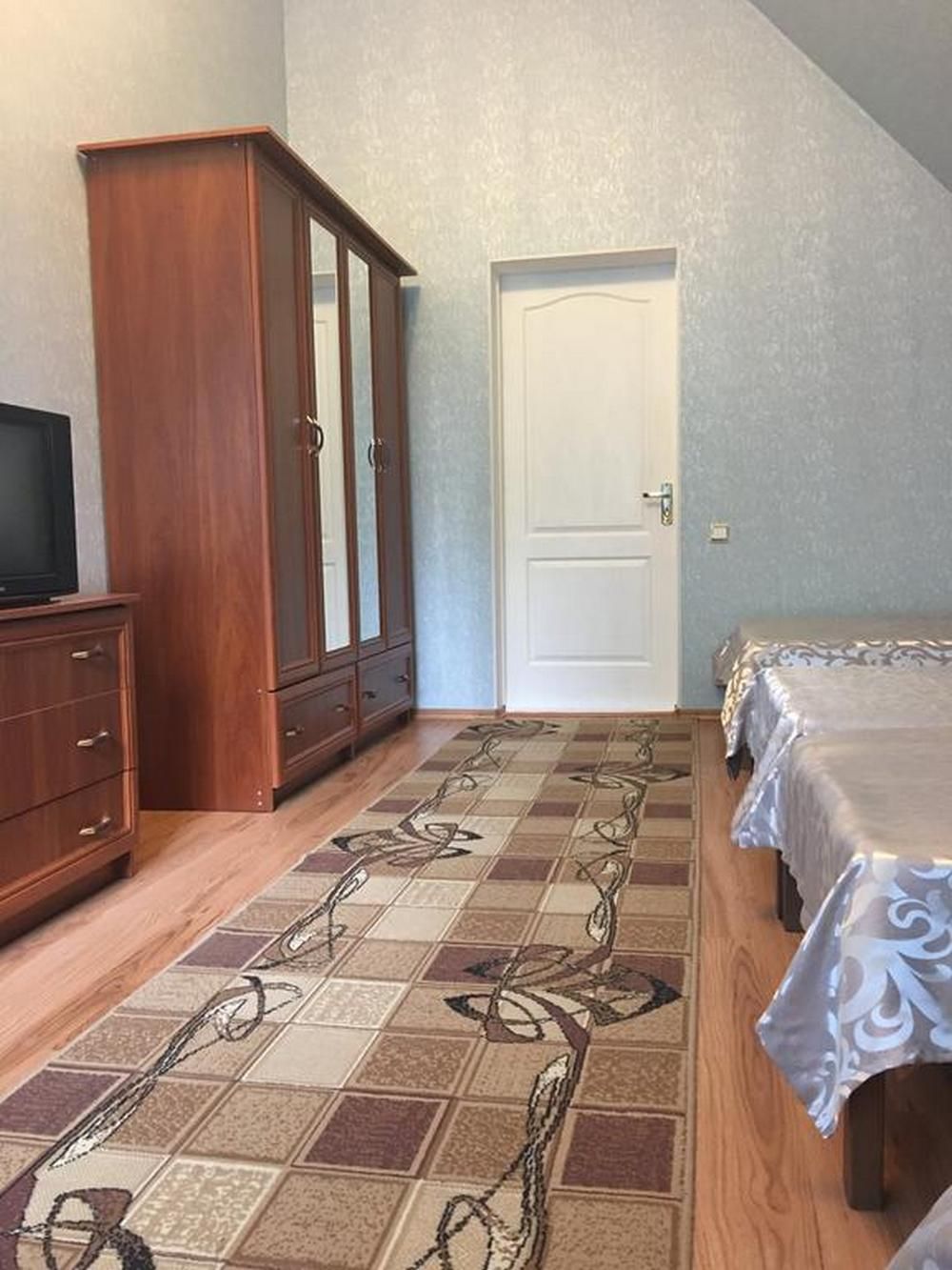 A bedroom with a wooden wardrobe, a bed with a patterned bedspread, and a door.