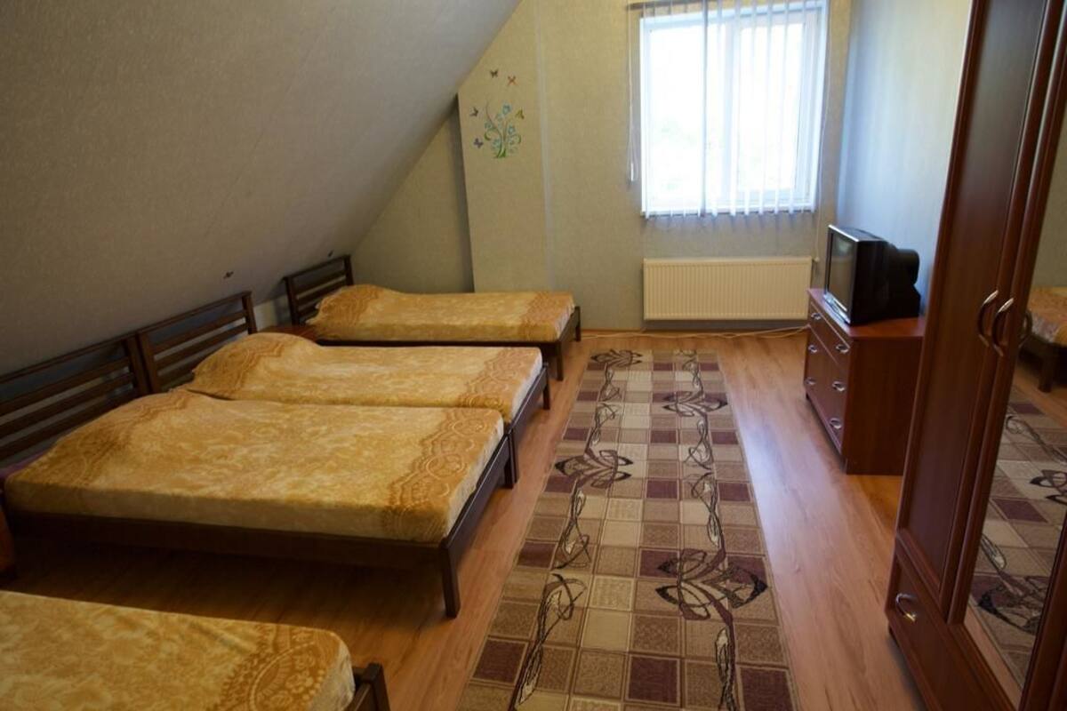 Quarto com três camas, um radiador, uma televisão e um tapete estampado.