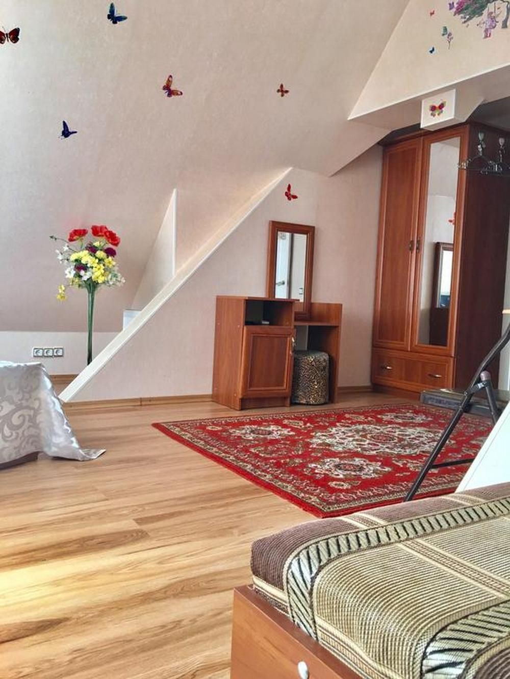 A room with a wooden floor, a red patterned rug, a sofa, a cabinet, and a mirror.