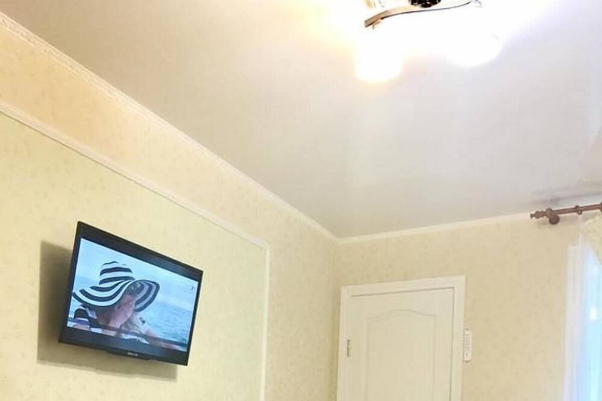 Quarto com duas camas, televisão fixada na parede, uma porta branca e uma cadeira.