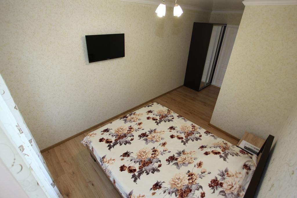 A bedroom with a bed, a flat-screen TV mounted on the wall, and a door leading to another room.