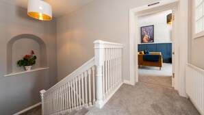 A hallway with a white railing, a potted plant, and a framed artwork on the wall. - Hamilton House Holiday Apartments (Downpatrick)