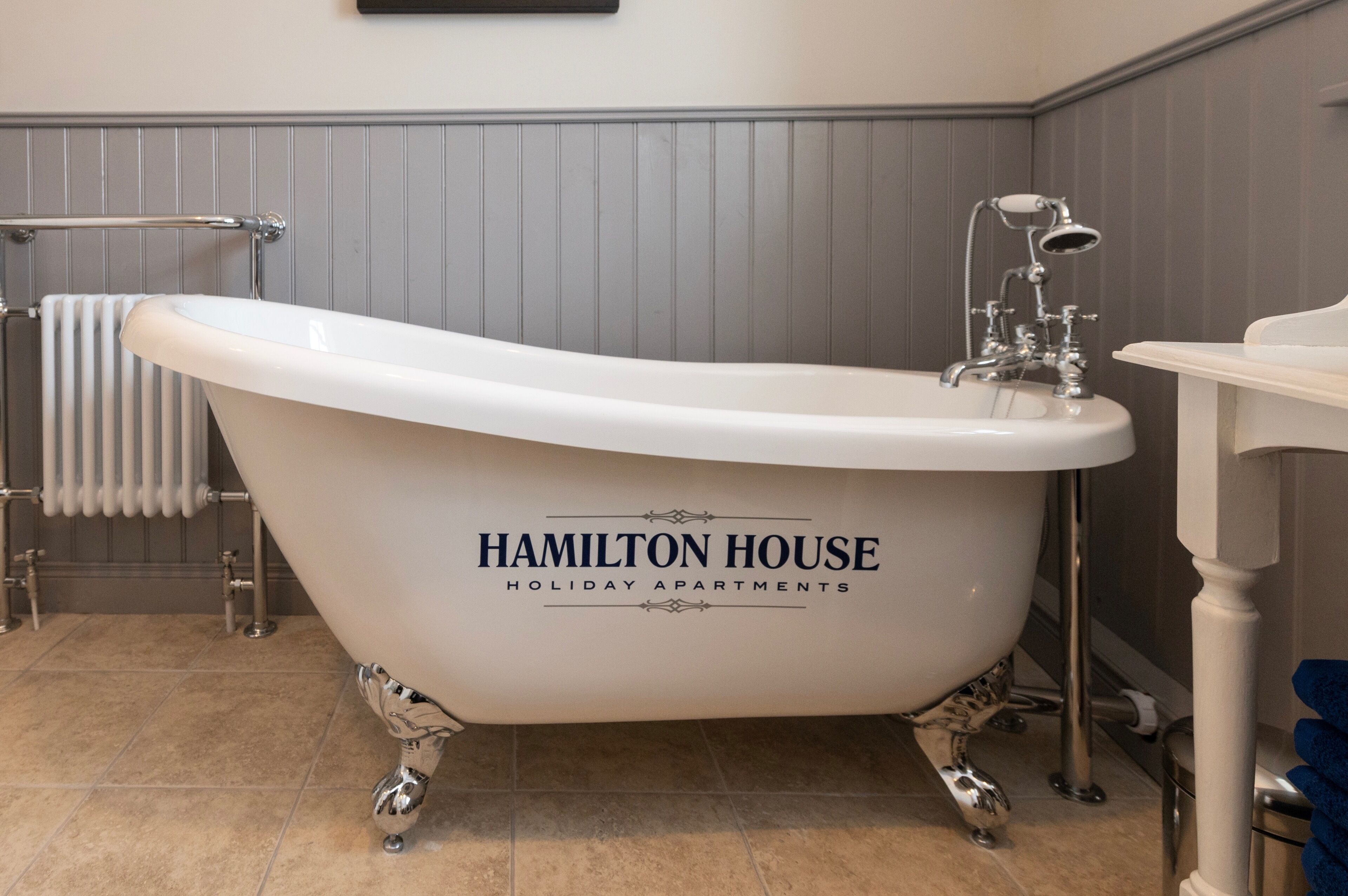 Une salle de bain avec une baignoire sur pieds, sur laquelle est apposée une étiquette indiquant « Hamilton House Holiday Apartments ».