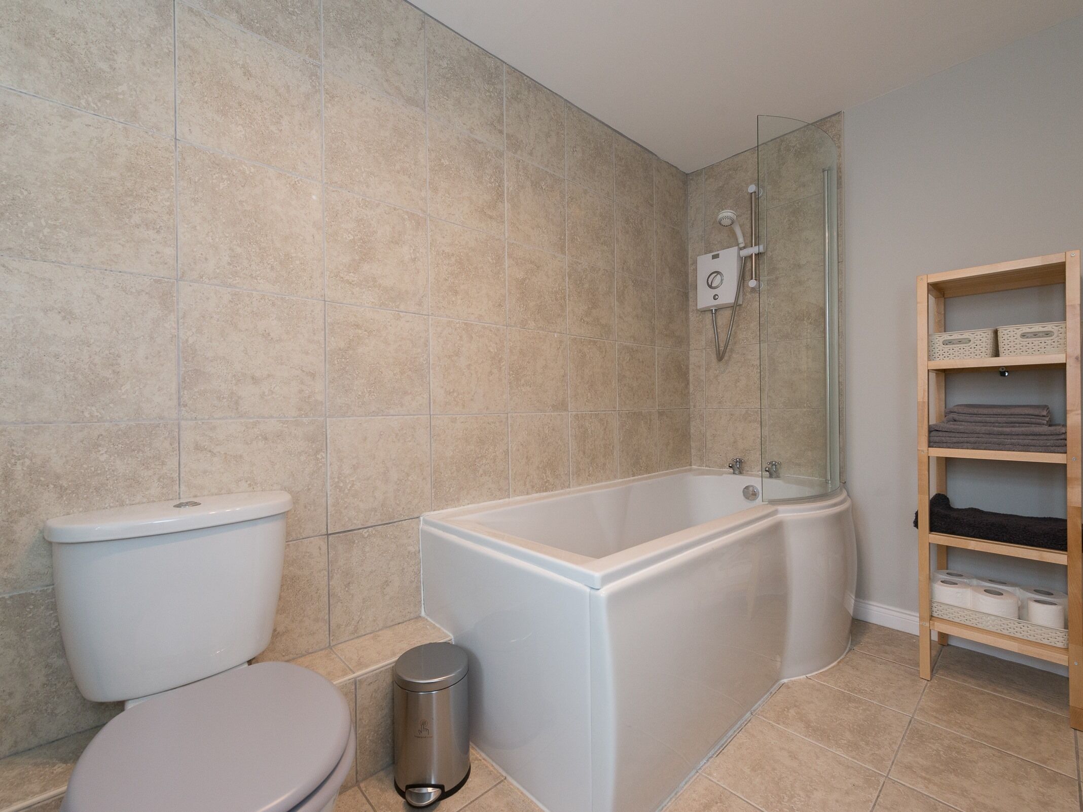 Une salle de bain équipée de toilettes, d’une baignoire, d’une douche et d’une étagère où sont rangées les serviettes.