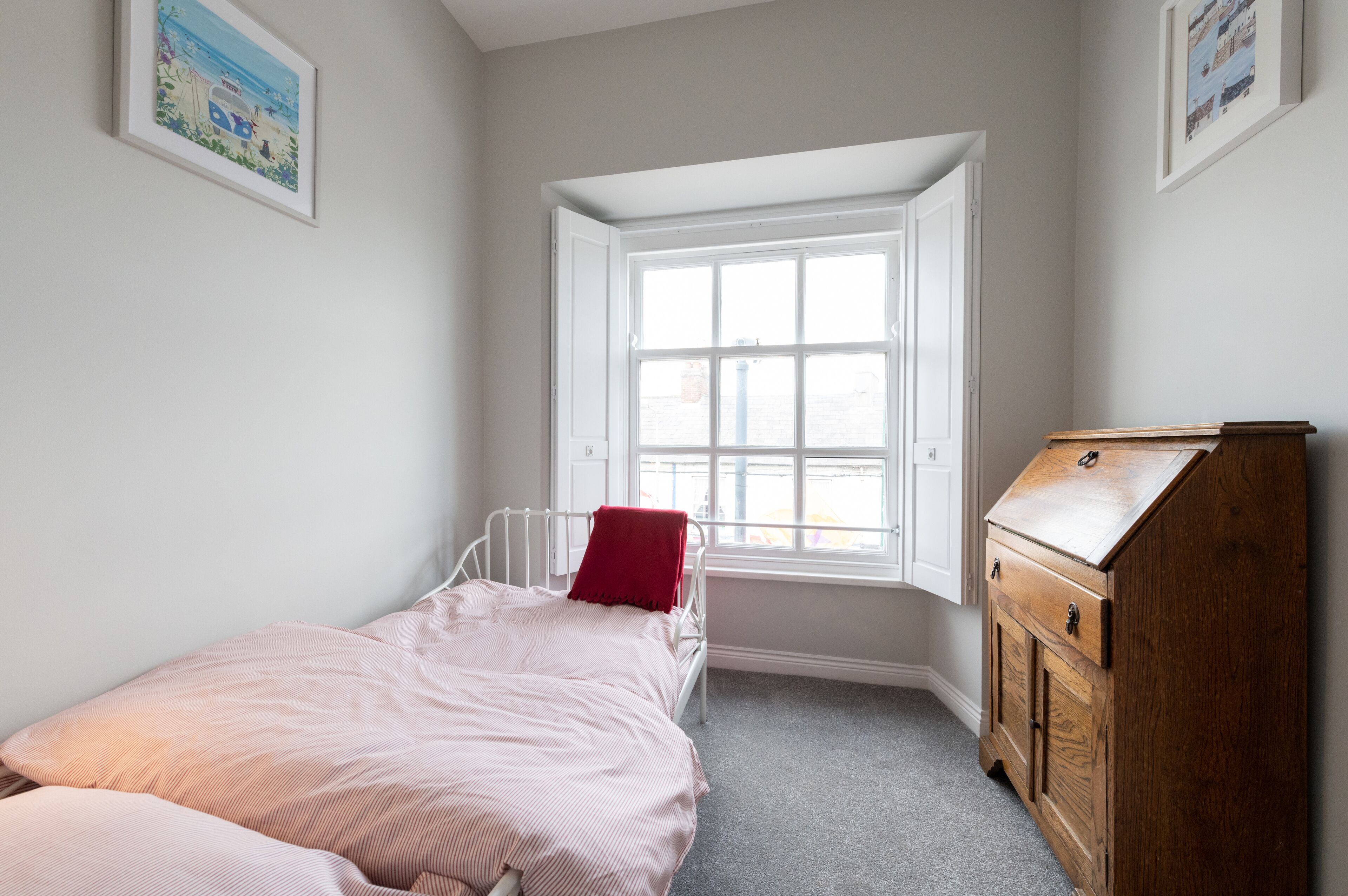 A bedroom with a single bed, a window, and a wooden dresser.
