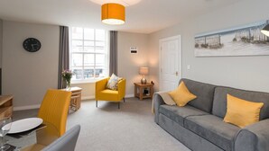 A modern living room with a grey sofa, yellow armchair, and a dining area with a table and chairs. - Hamilton House Holiday Apartments (Downpatrick)