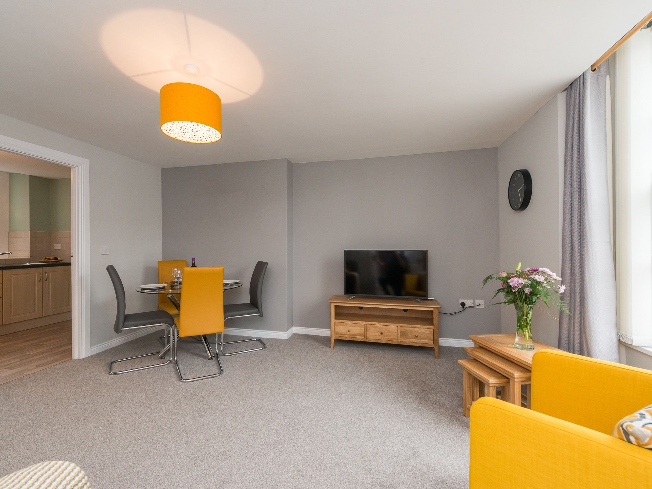 A modern living room with a dining area, a flat-screen TV, and a wooden cabinet.