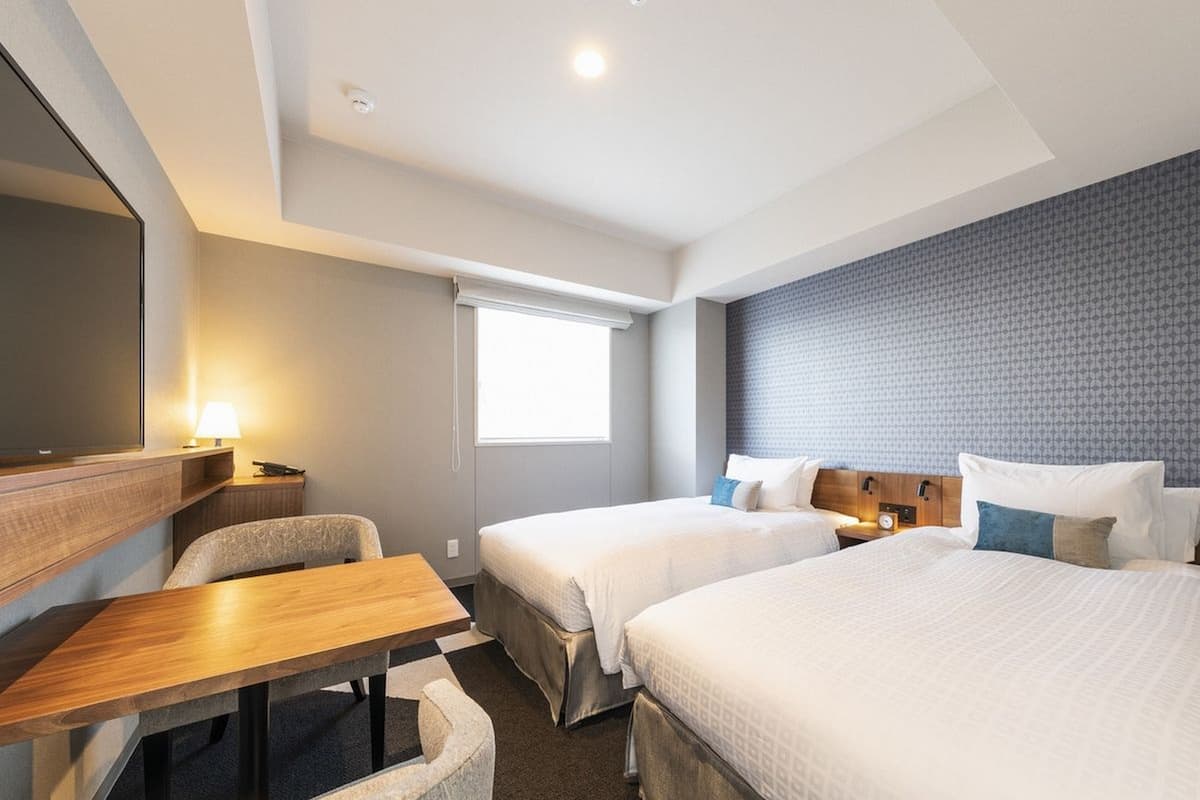 Une chambre d’hôtel avec deux lits, un bureau, une chaise, une télévision et une fenêtre.
