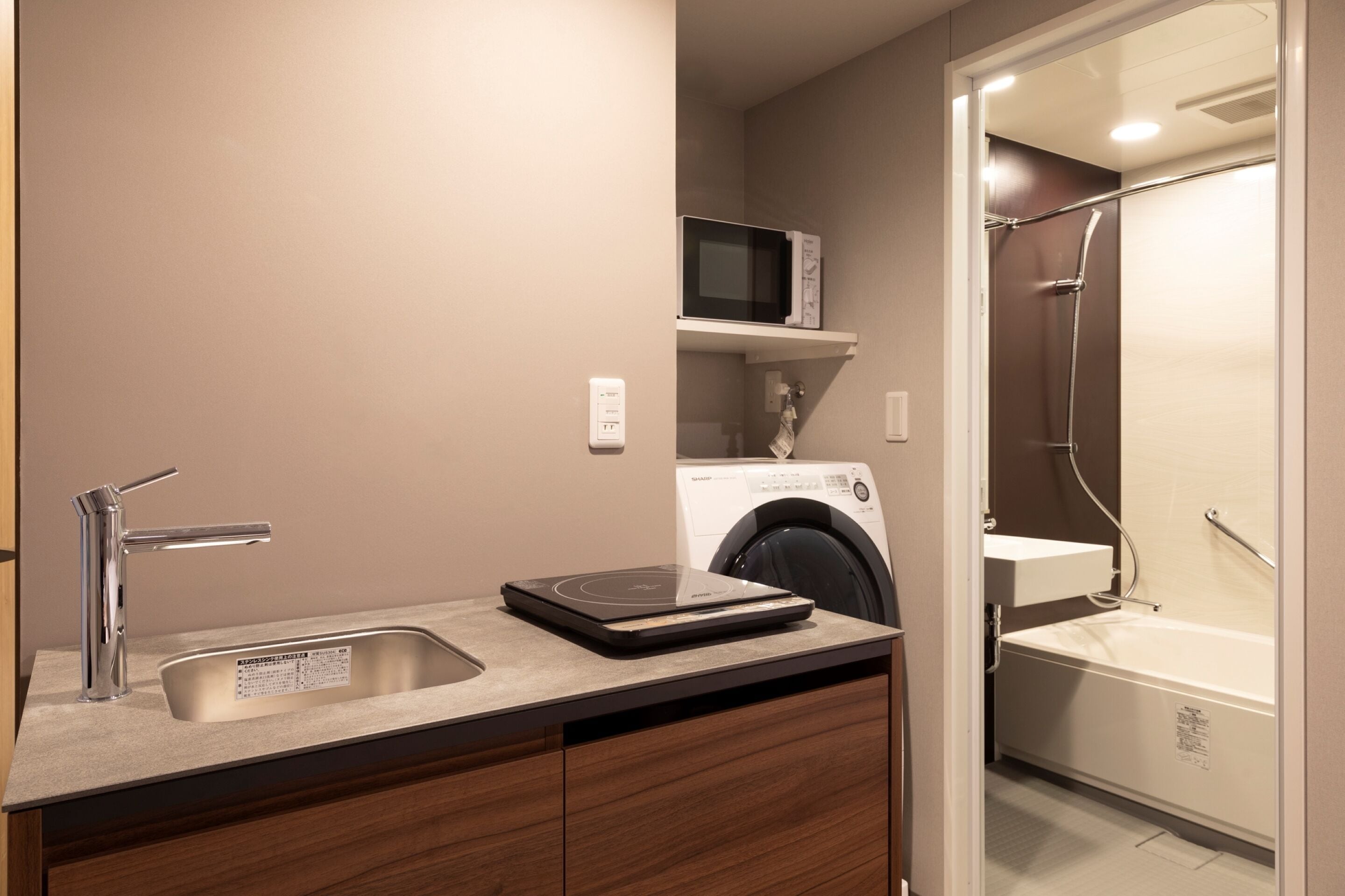A modern bathroom with a sink, microwave, washing machine, and a shower area.