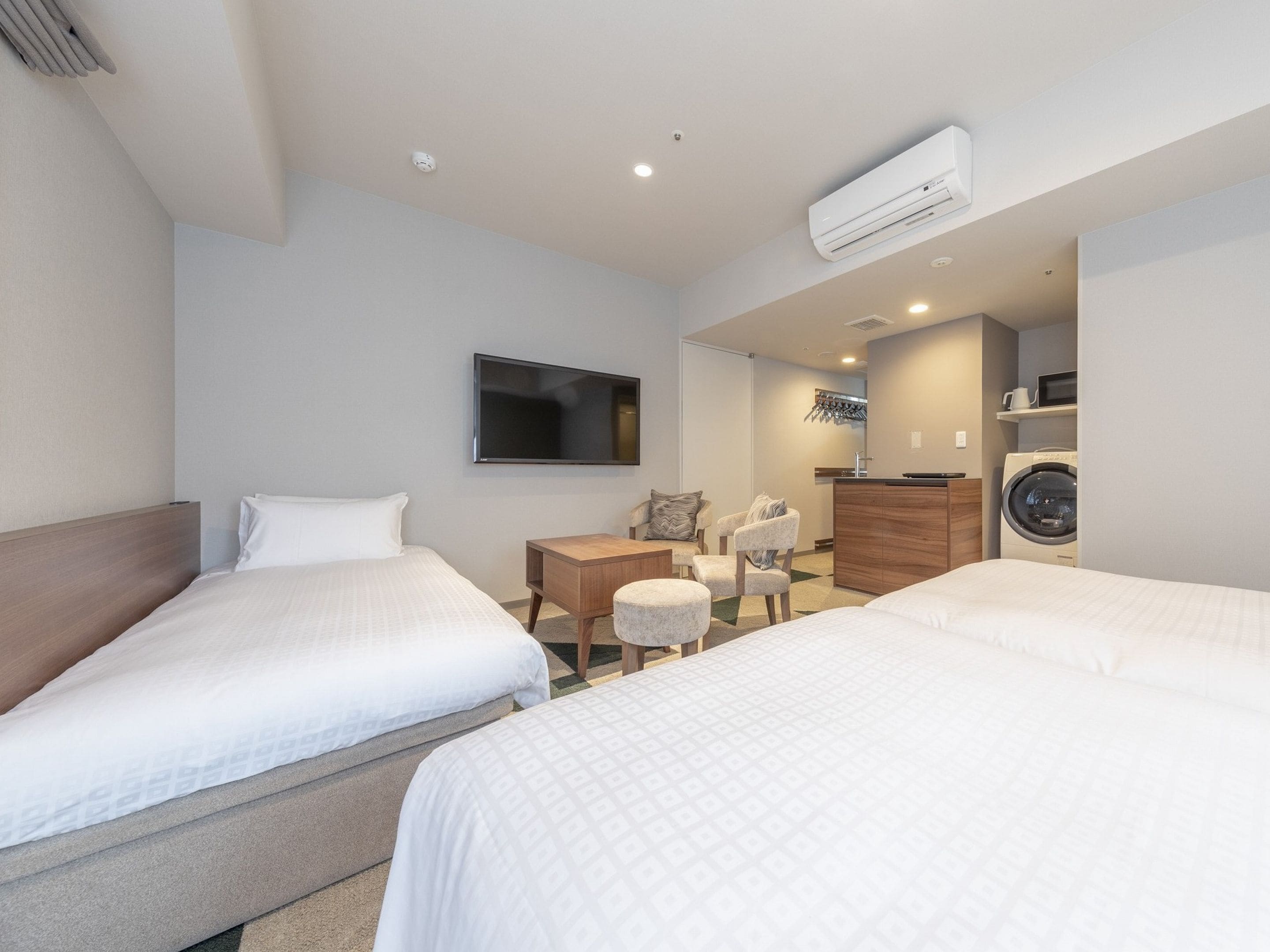 A hotel room with two beds, a desk, a chair, a TV, and a washing machine.
