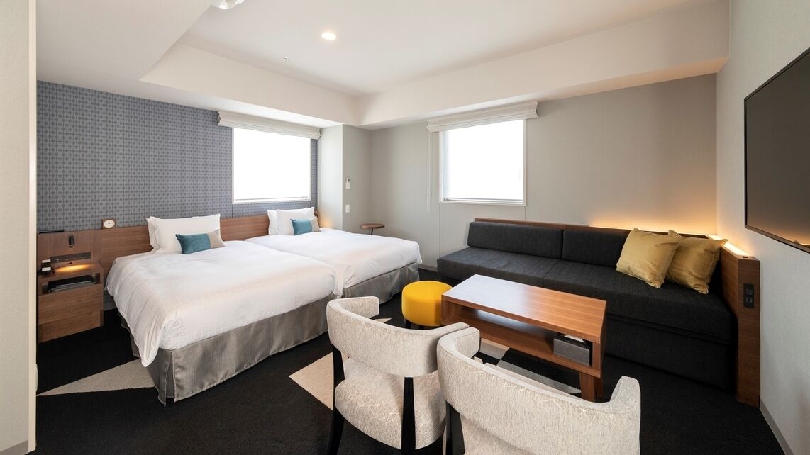 Une chambre d’hôtel moderne avec deux lits, un canapé, une petite table et un téléviseur.
