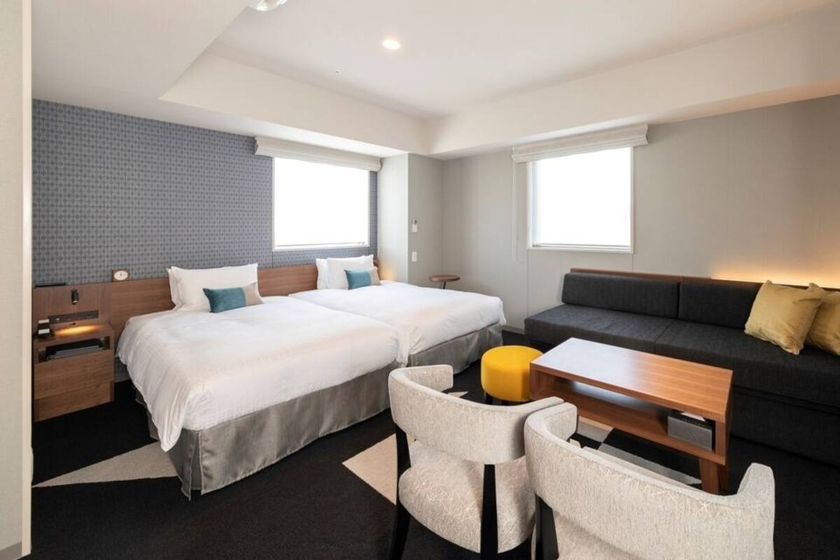 Une chambre d’hôtel moderne avec deux lits, un canapé, une petite table et un téléviseur.