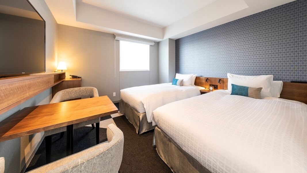Une chambre d’hôtel avec deux lits, un bureau, une chaise, une télévision et une fenêtre.